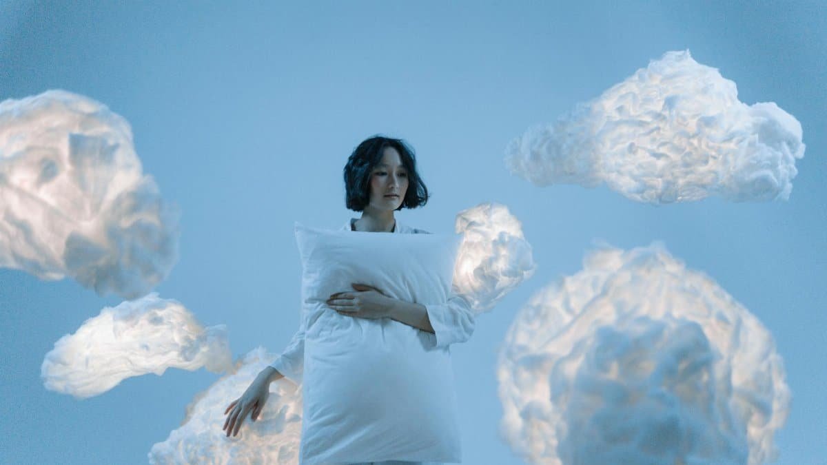 A serene portrait of a woman holding a pillow surrounded by soft clouds, evoking a dreamlike atmosphere.