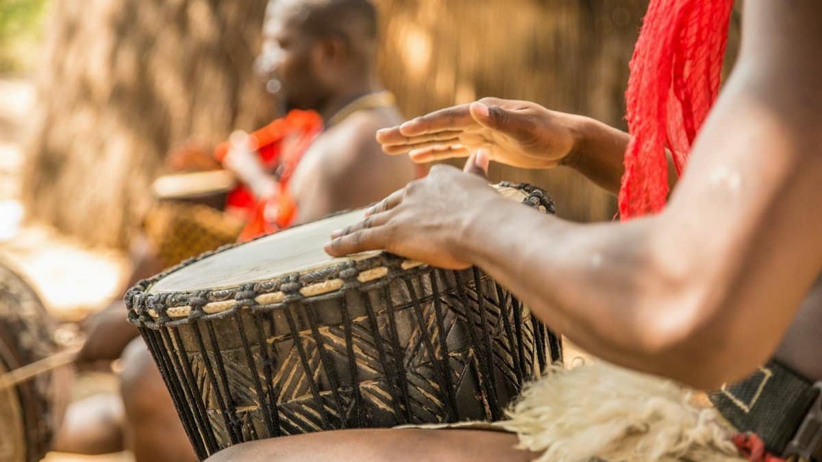 Close-up of a person playing a traditional African drum in an outdoor setting.