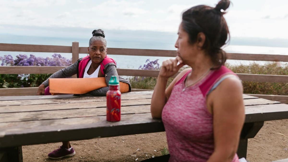 Two women resting by the beach after yoga, enjoying a serene outdoor setting.
