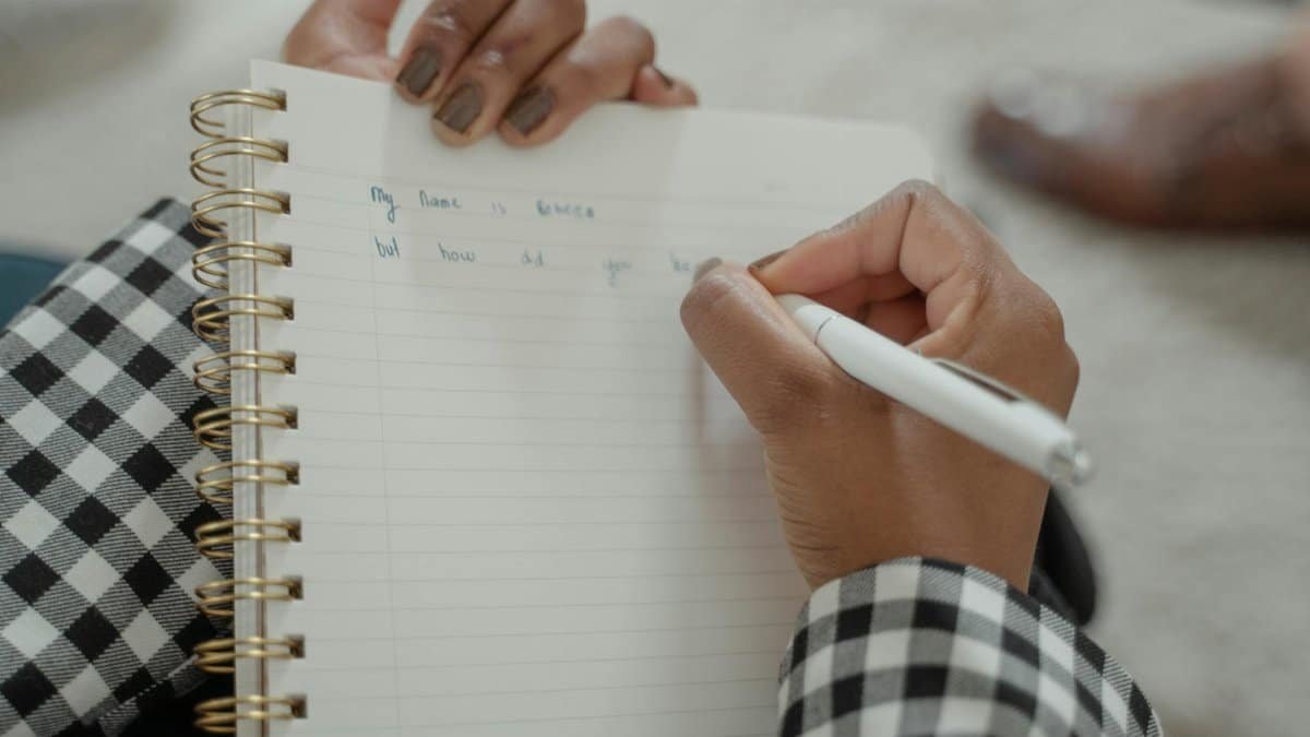 A person writing with a pen on a spiral notebook, close-up view.