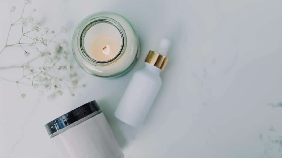 Overhead view of spa essentials including a candle, dropper bottle, and jar on a white marble surface.