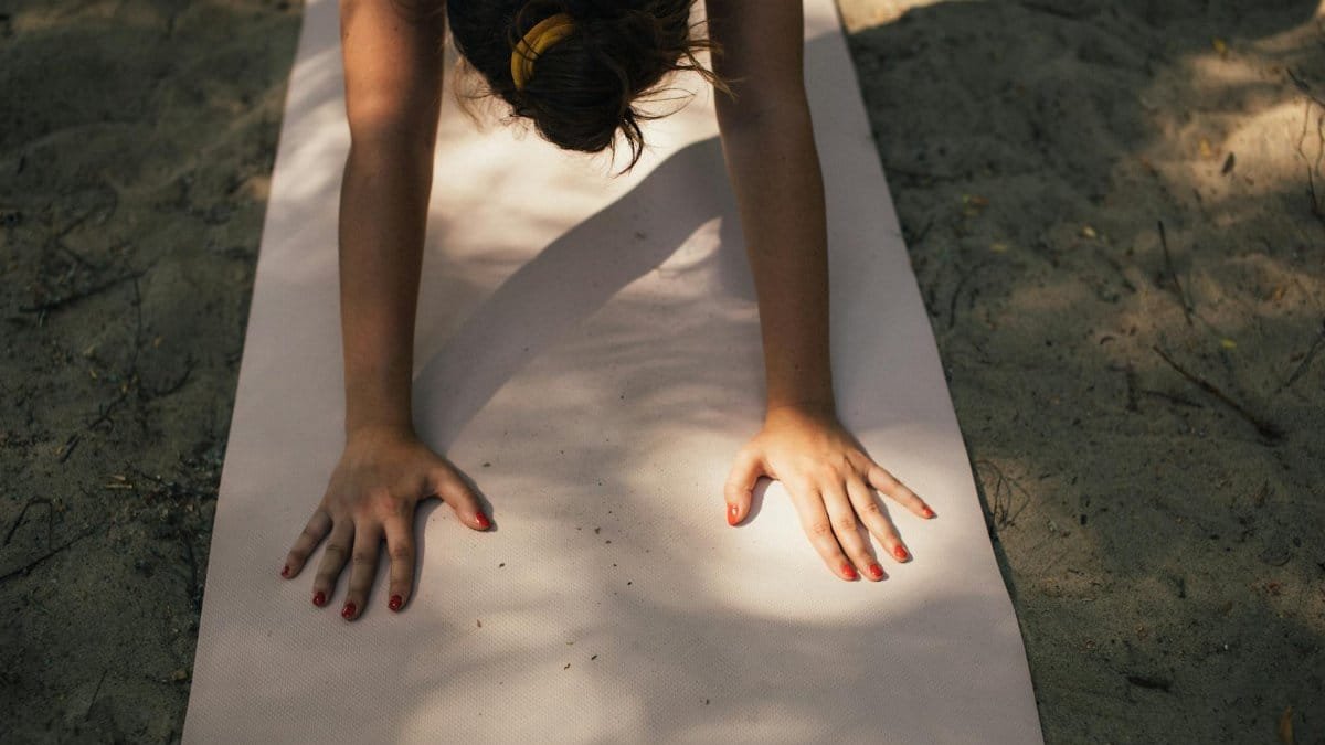 A woman exercises on a yoga mat in outdoor sunlight, promoting fitness and relaxation.