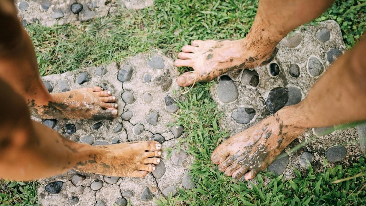 Two adults with muddy feet on a stone path enjoying an outdoor experience.