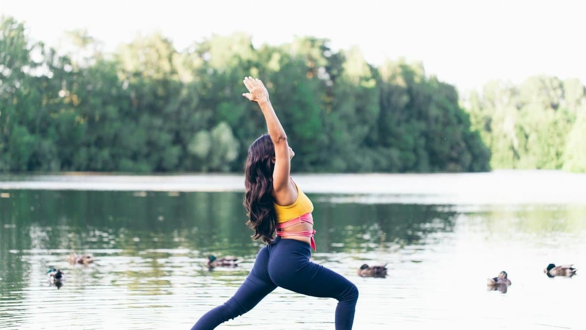 Woman doing yoga by a lake, surrounded by nature, embodying serenity and fitness.