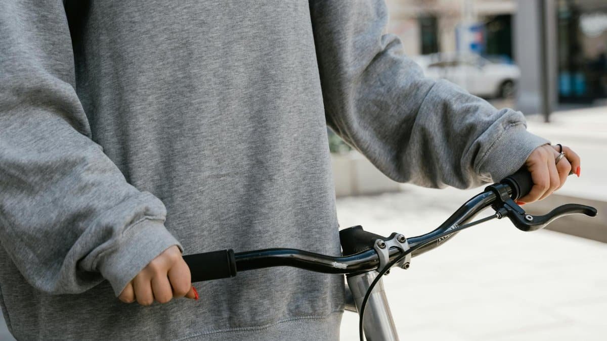 A person in casual attire gripping bicycle handlebars in an outdoor urban setting.