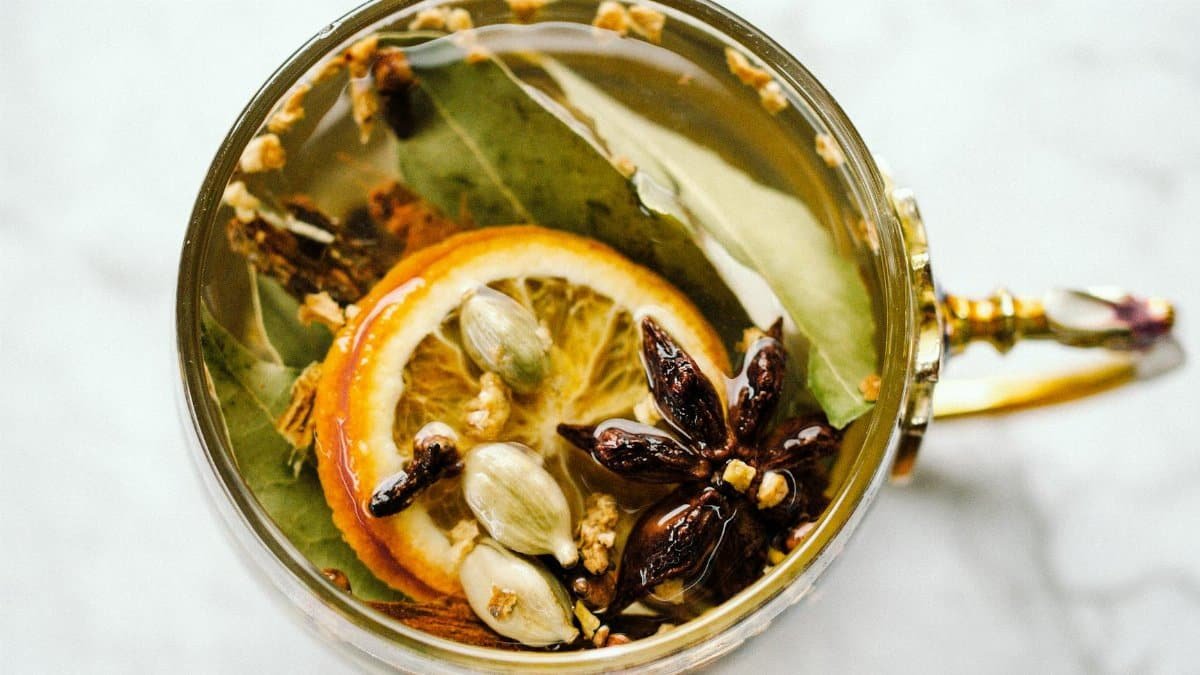 A top-view of herbal tea with citrus slices, star anise, and cardamom in an ornate cup.