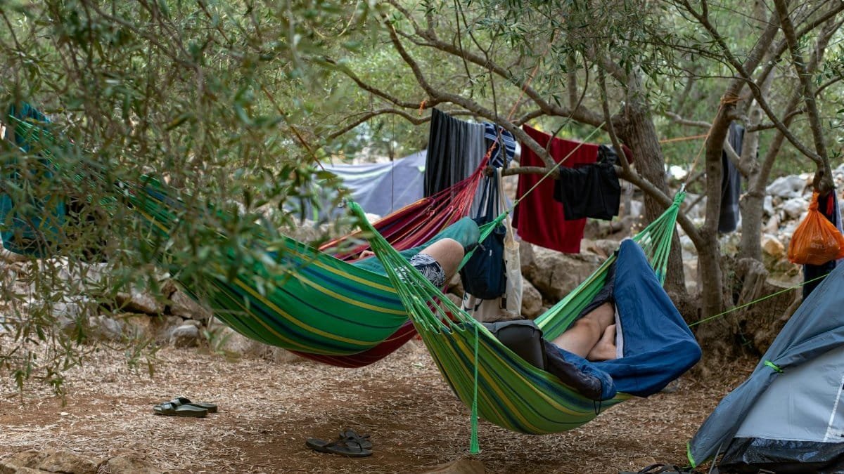 Two campers relaxing in hammocks amidst trees at Lastovo campsite, Croatia.