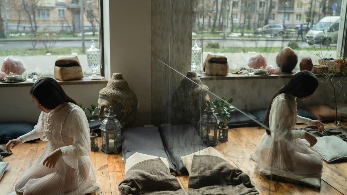 A woman meditates in a tranquil, sunlit room adorned with crystals and plants. Reflection adds depth.