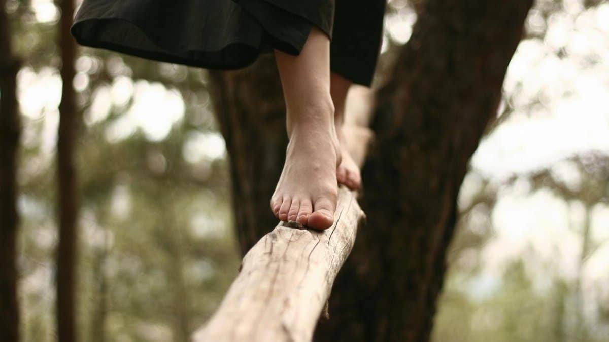 A woman walks barefoot on a log in a serene forest setting, capturing balance and focus.