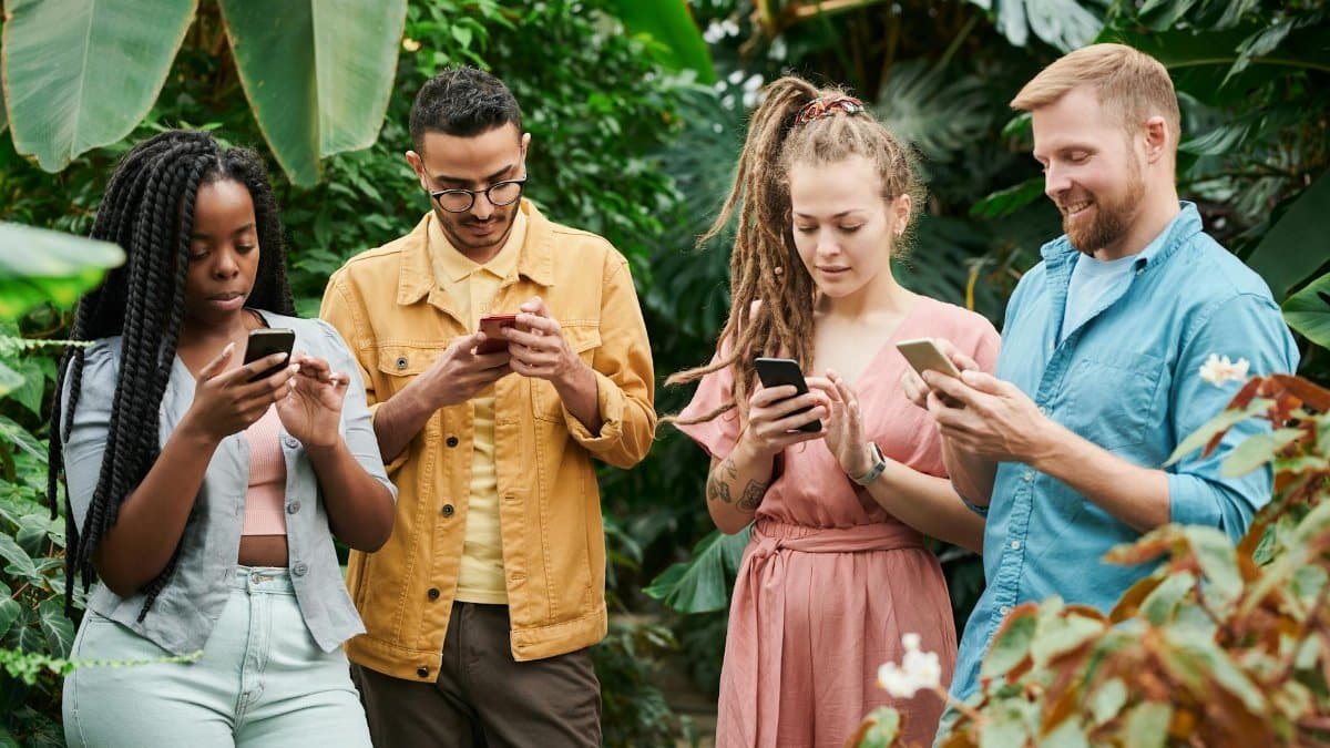 Four adults using smartphones surrounded by lush greenery in an outdoor setting, enjoying technology in nature.