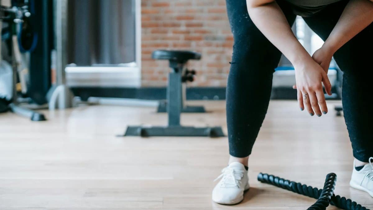 Crop anonymous female in sportswear resting after workout with ropes in gym with sports equipment