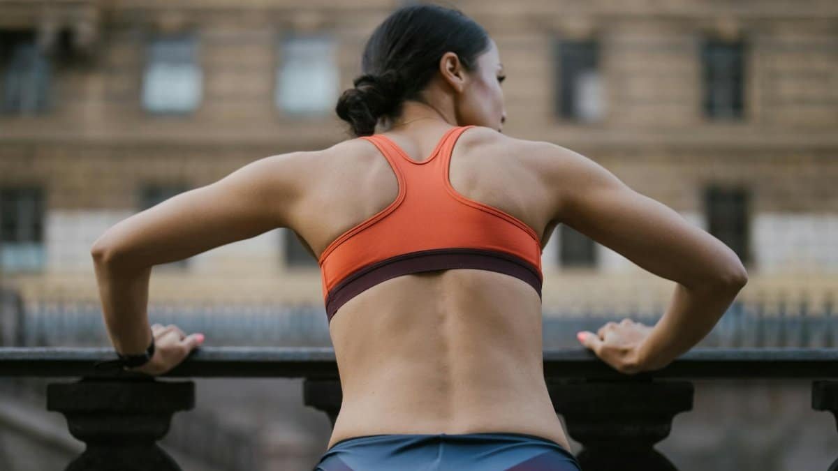 Back view of a woman in activewear working out outdoors on a balcony.
