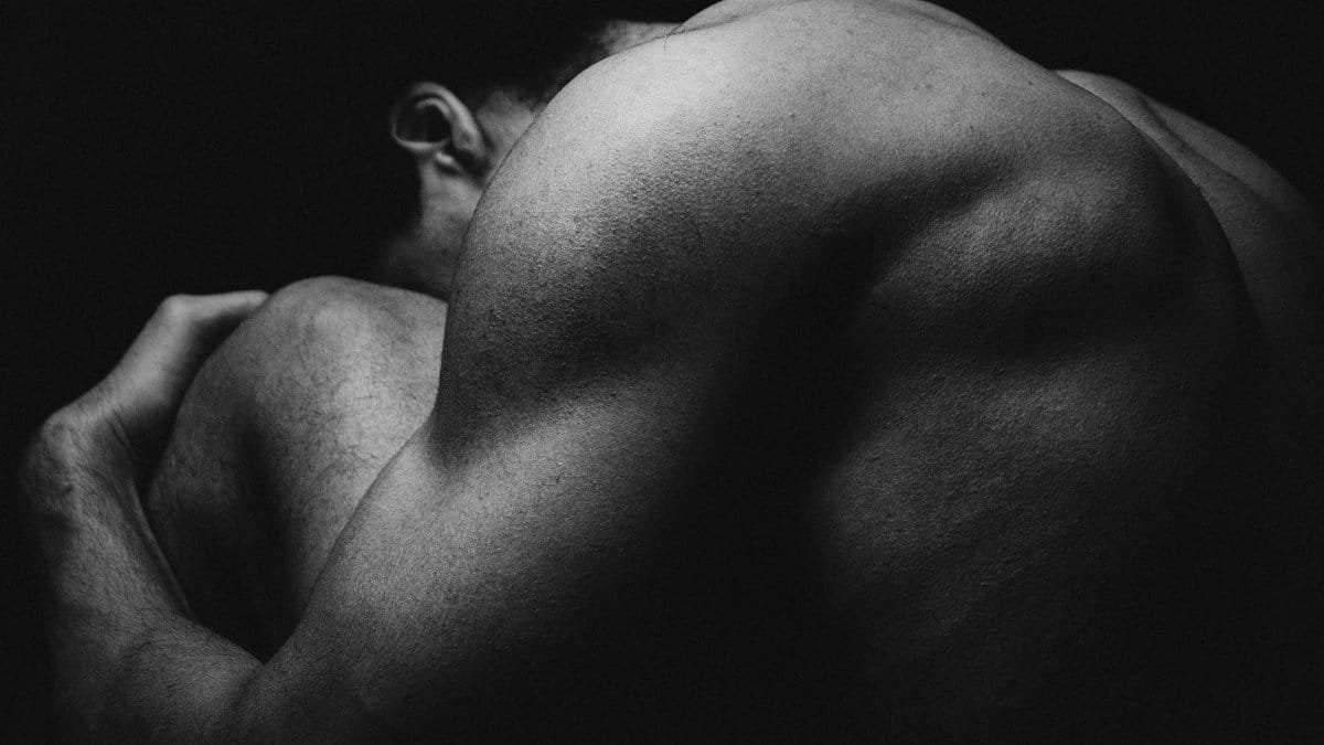 Abstract black and white photo highlighting muscular anatomy and shadows in a studio setting.