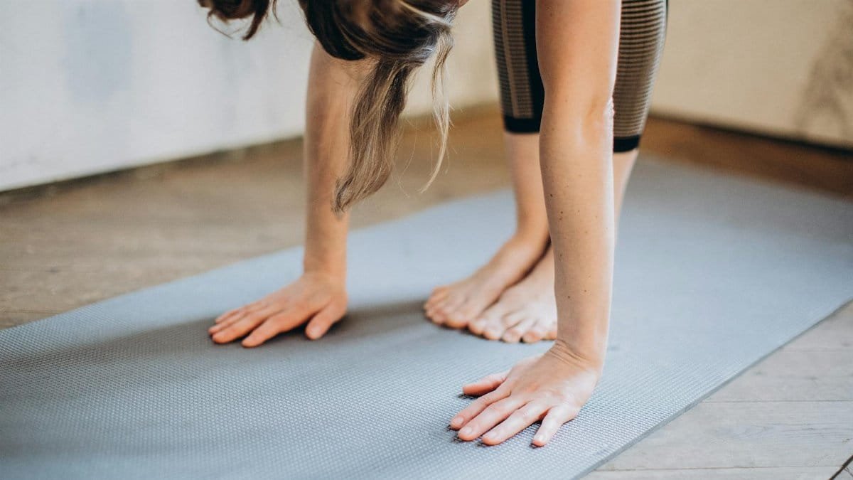An adult woman performing a forward bend yoga pose indoors on a mat, focusing on flexibility and concentration.