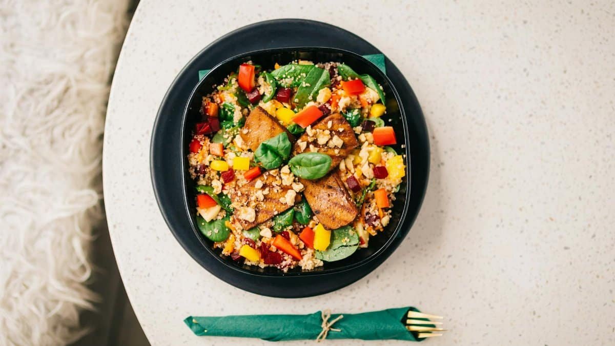 Colorful quinoa salad in black bowl on white table, garnished with grilled veggies.