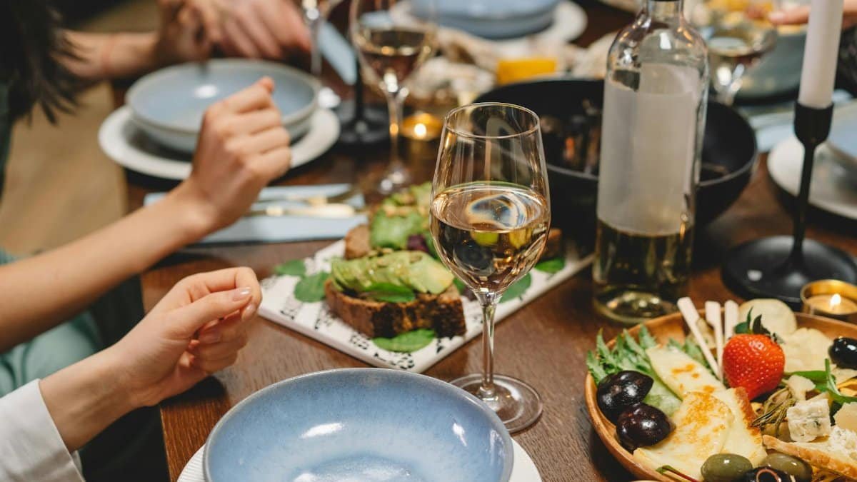 Close-up of a dinner table with wine, appetizers, and people enjoying a meal in a cozy indoor setting.