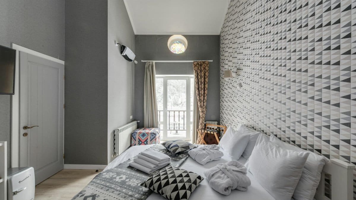 Stylish bedroom featuring geometric wallpaper, cozy bed, and natural light.