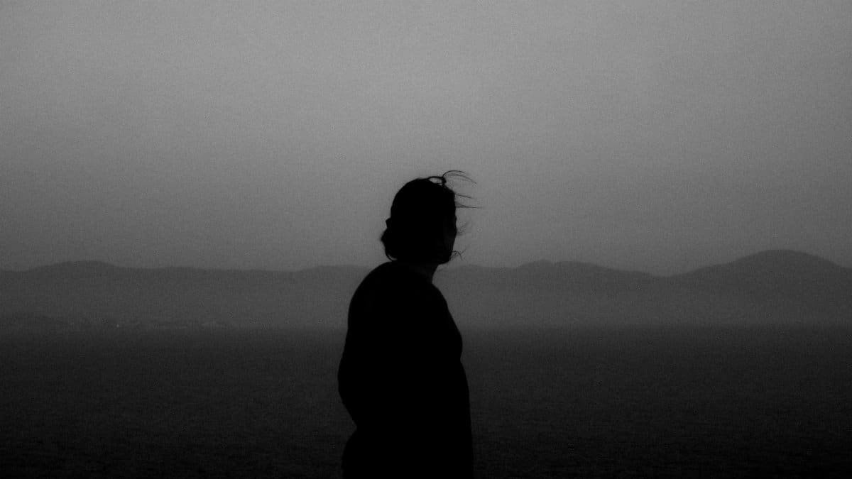 A serene silhouette of a woman gazing at misty mountains during sunrise.