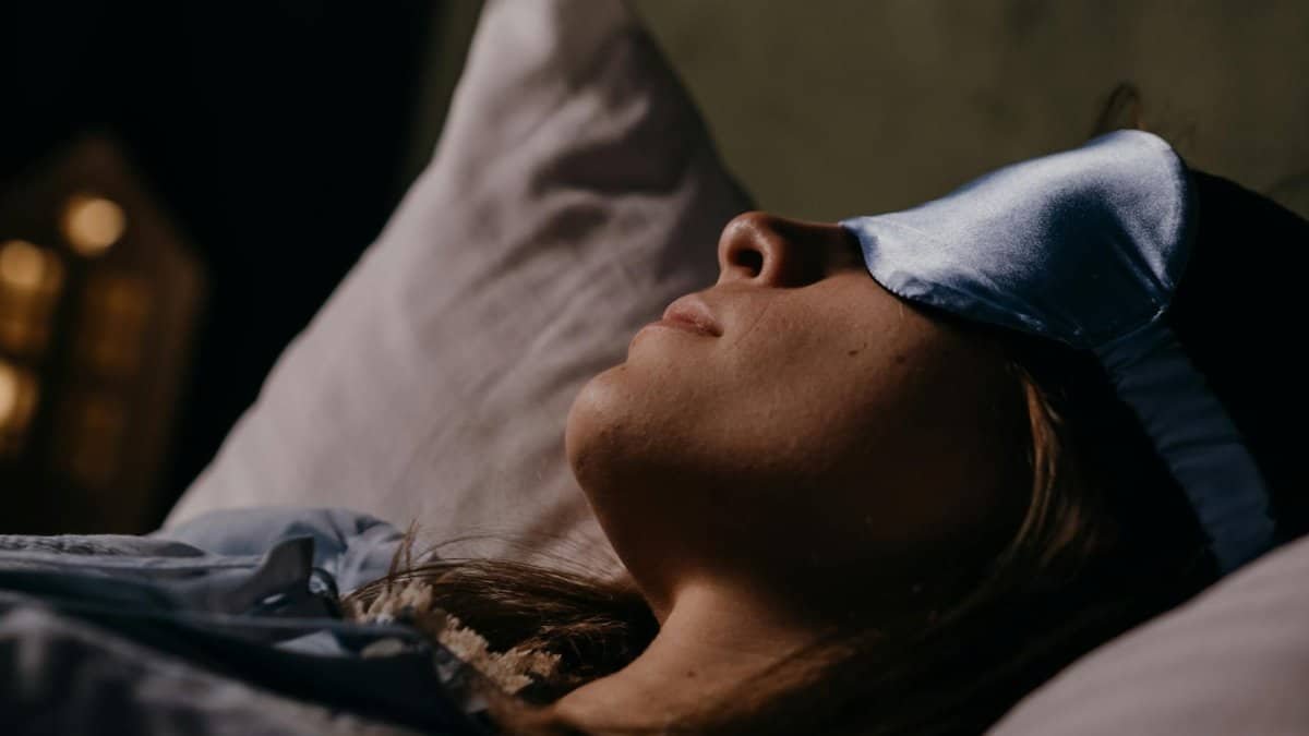 A serene scene of a woman wearing a blue eye mask, sleeping soundly in a cozy indoors setting.