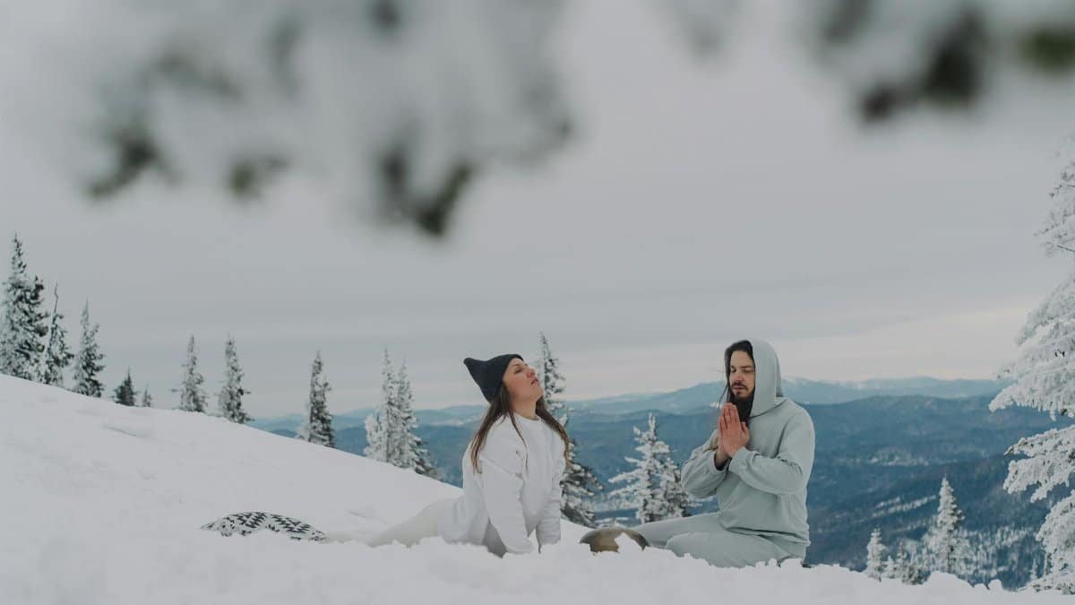 A couple meditating peacefully on snow-covered mountains, reflecting winter tranquility.