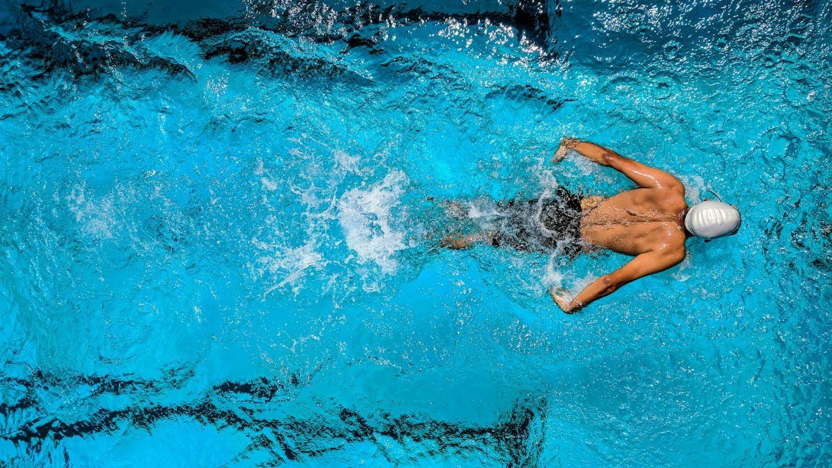 Top view of a swimmer wearing a cap, performing a front crawl stroke in a clear blue swimming pool.