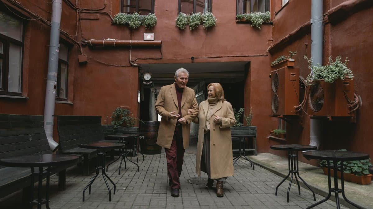 Senior couple walking arm in arm in a cozy courtyard, enjoying a winter day.