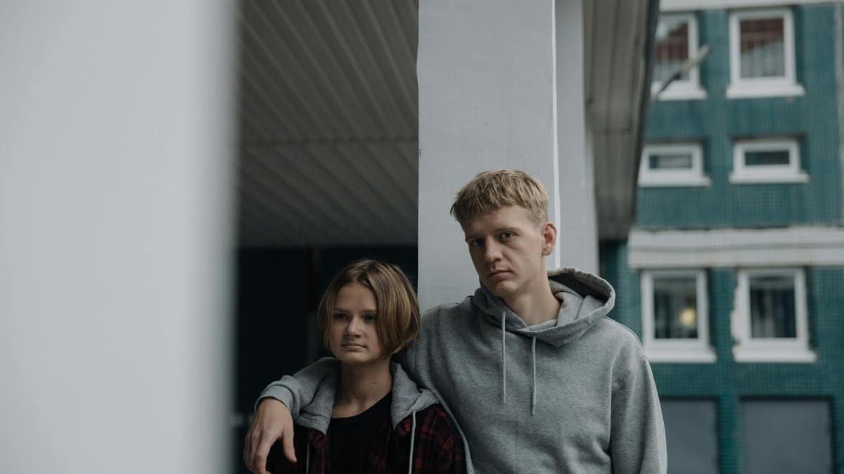 Two siblings in casual wear leaning against a pillar, showcasing a relaxed urban vibe.