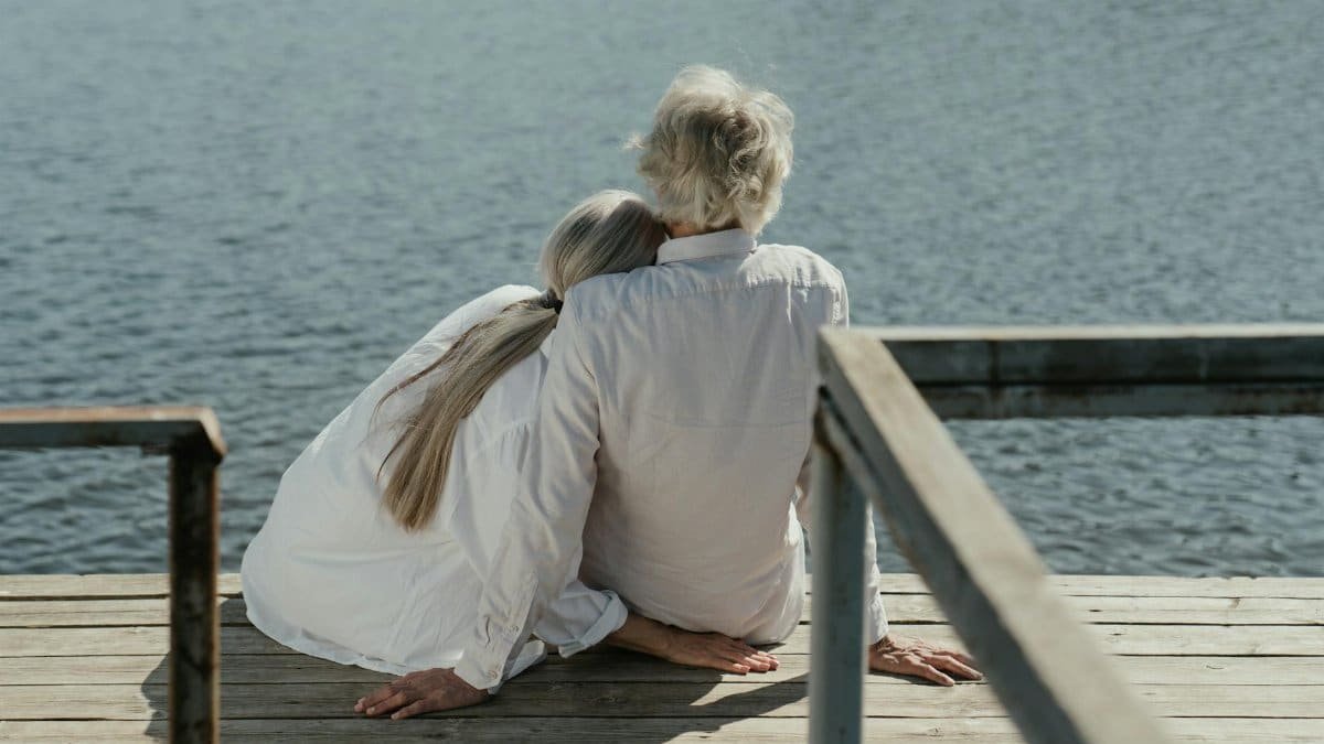 A senior couple enjoys a peaceful moment sitting together on a wooden dock by the lake, symbolizing enduring love.