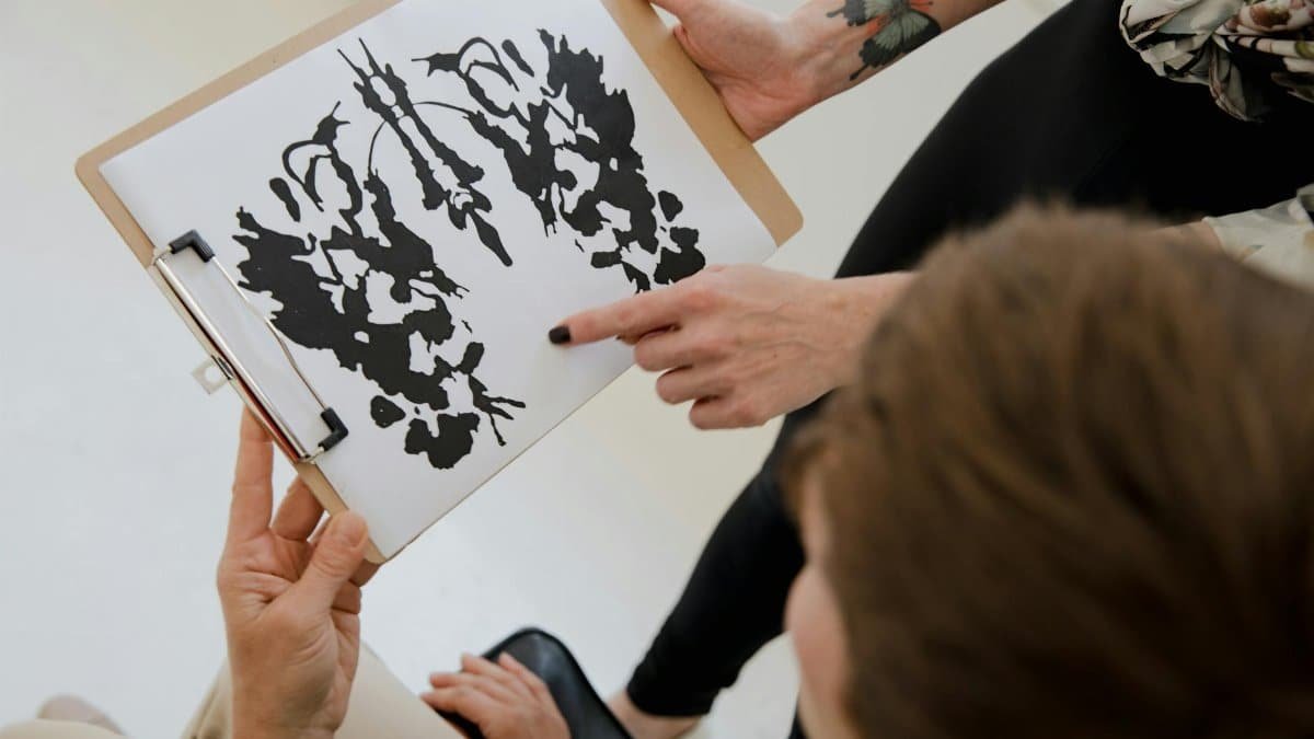 Hands holding a clipboard with an inkblot for psychological analysis.