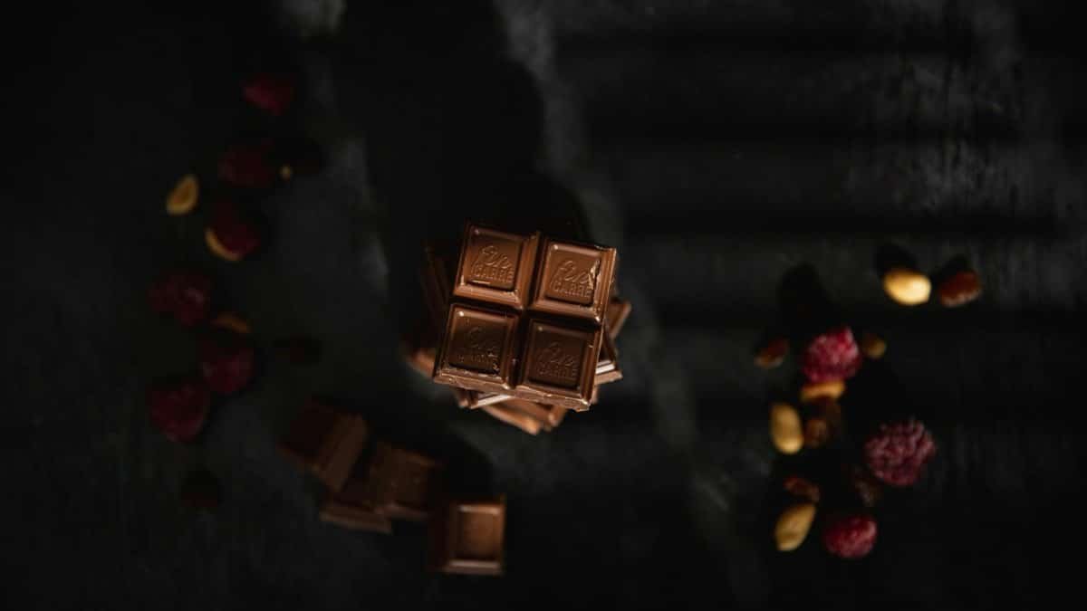 High-angle view of stacked chocolate bars with nuts and berries on a dark surface, featuring dramatic lighting.