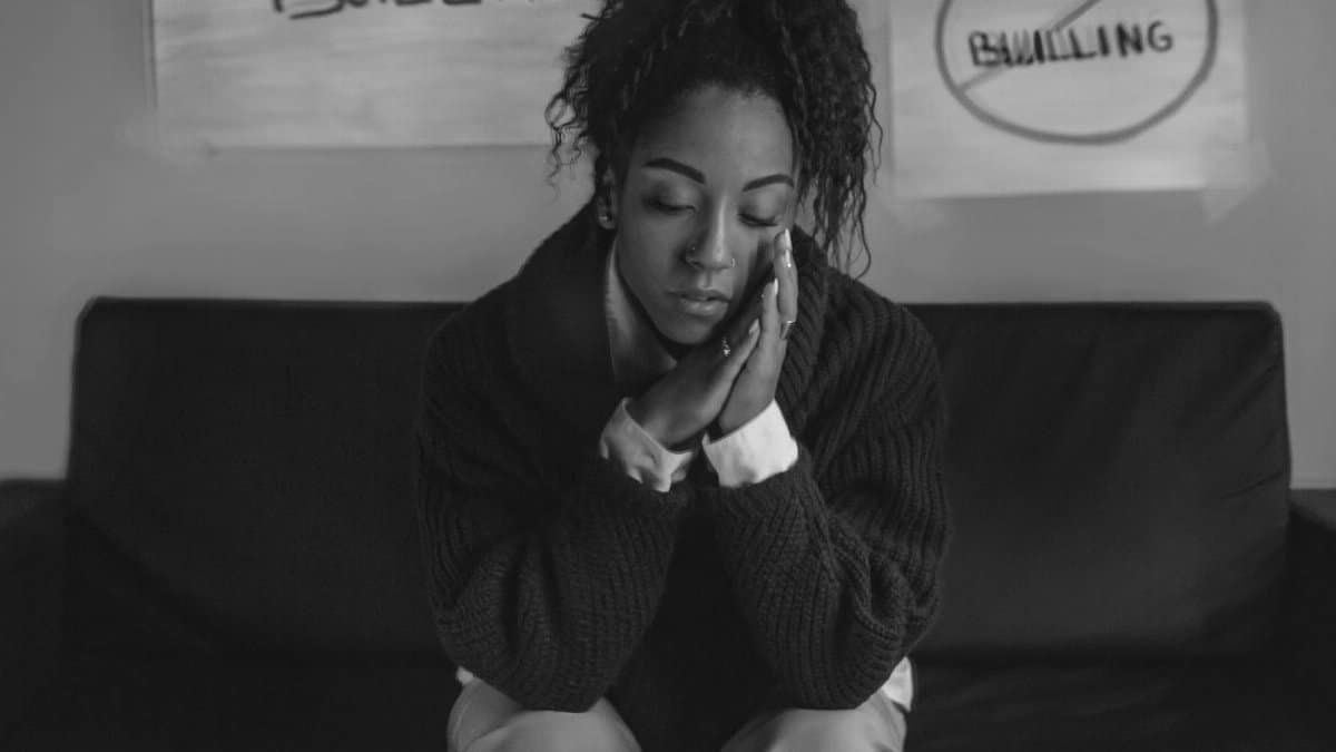 A young woman sits reflectively in front of anti-bullying posters, conveying emotion and thought.
