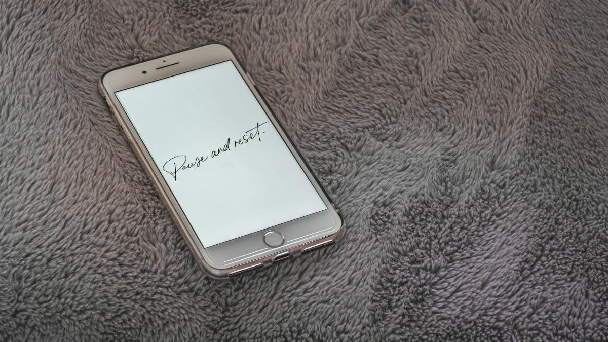 A smartphone displaying 'Pause and reset' message on a soft grey textured surface.