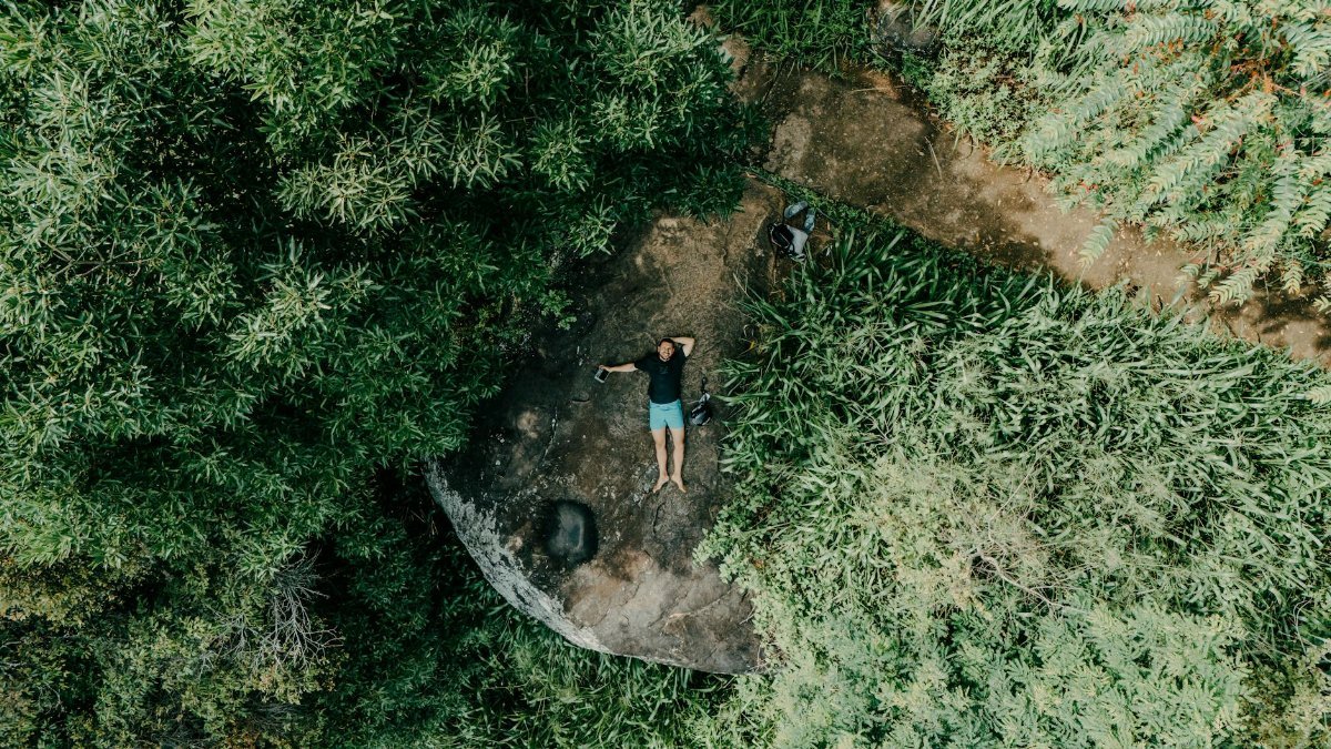 Aerial photo of a person lying on a rock surrounded by lush Sri Lankan jungle.