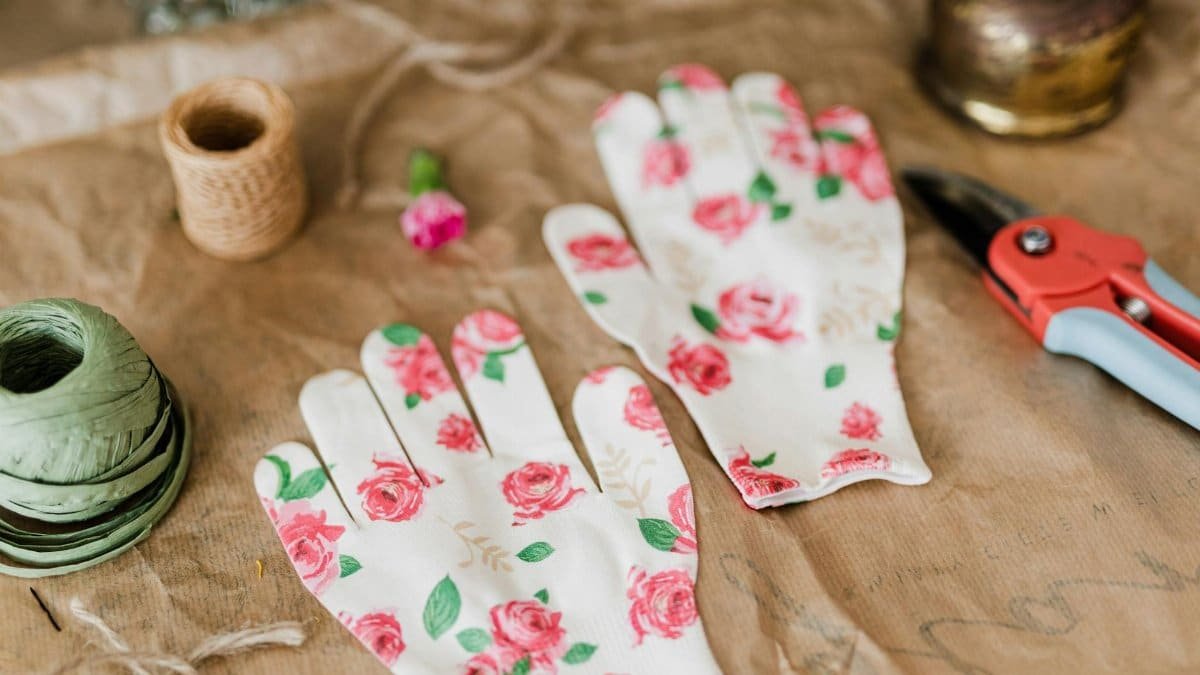 Pair of floral gloves with gardening tools and twine on a rustic table.