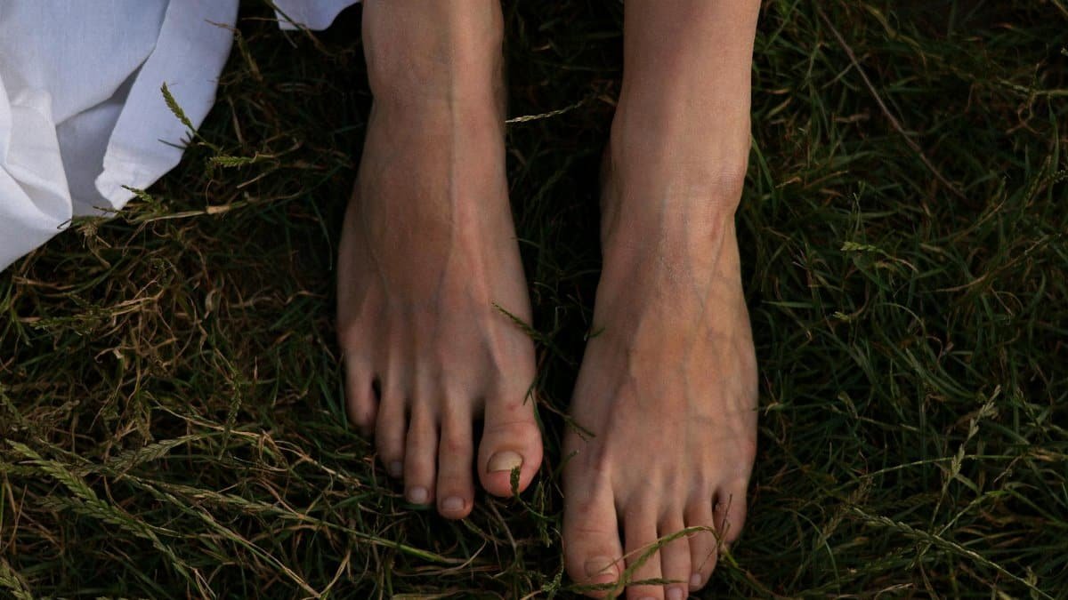 Close-up of a woman's bare feet in the grass, conveying a natural and serene summer vibe.