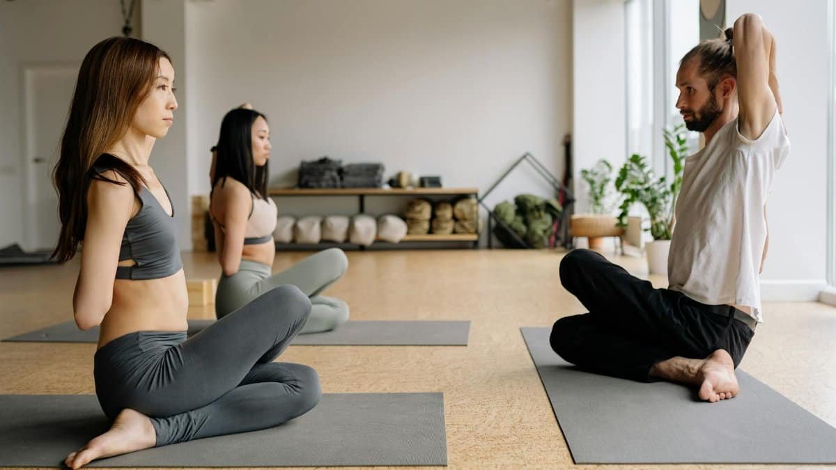 A mixed-gender group practicing yoga indoors, focusing on meditation and stretching.