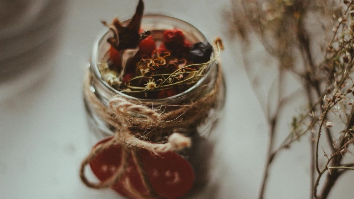 Warm still life of a glass jar with rustic herbal tea blend, tied with a string bow.