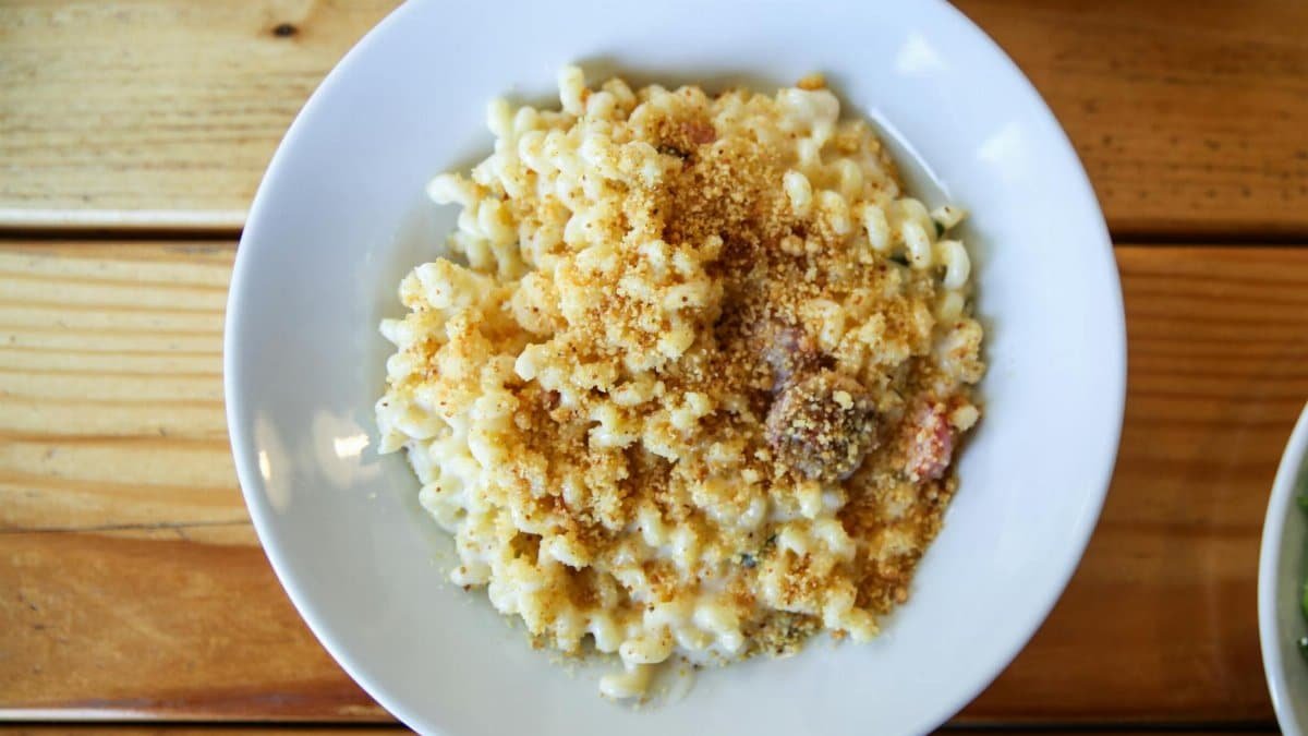 A close-up of creamy mac and cheese with breadcrumbs in a white bowl on a wooden table.