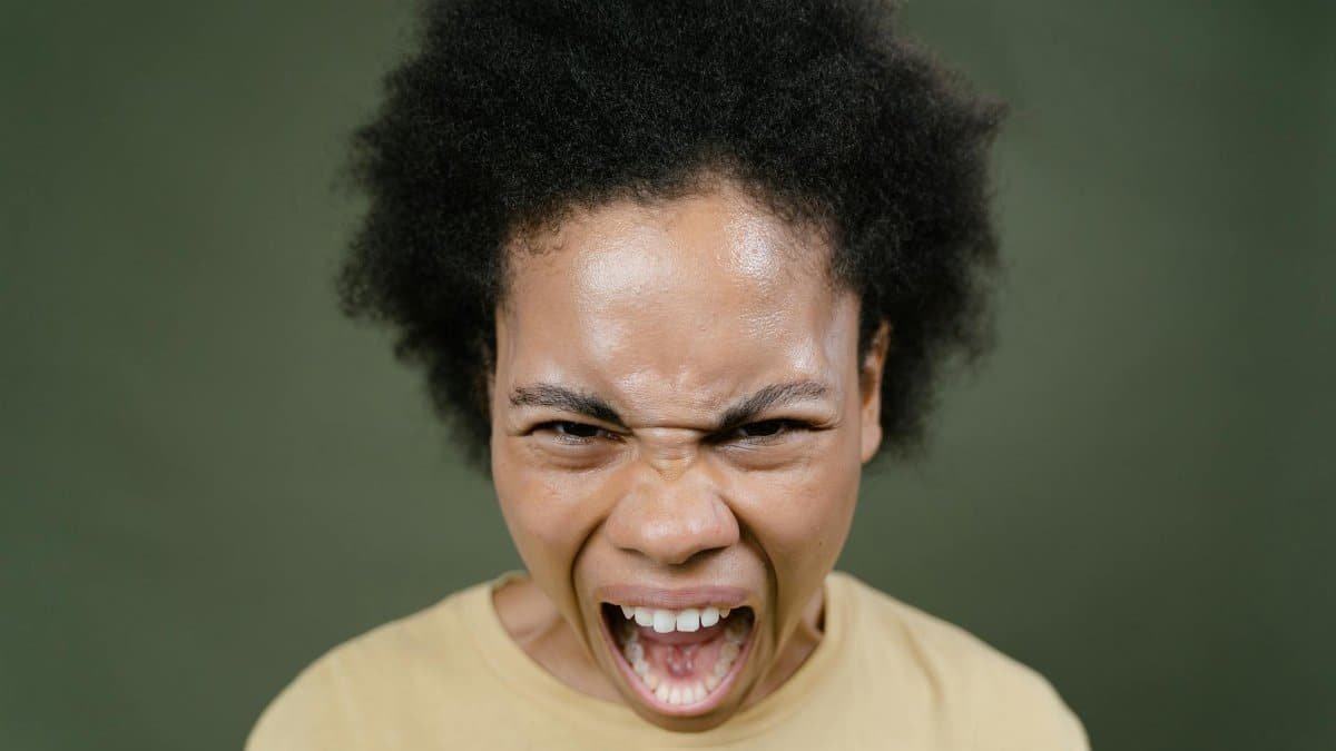 Close-up of an African American woman with afro hair expressing anger in a studio setting.