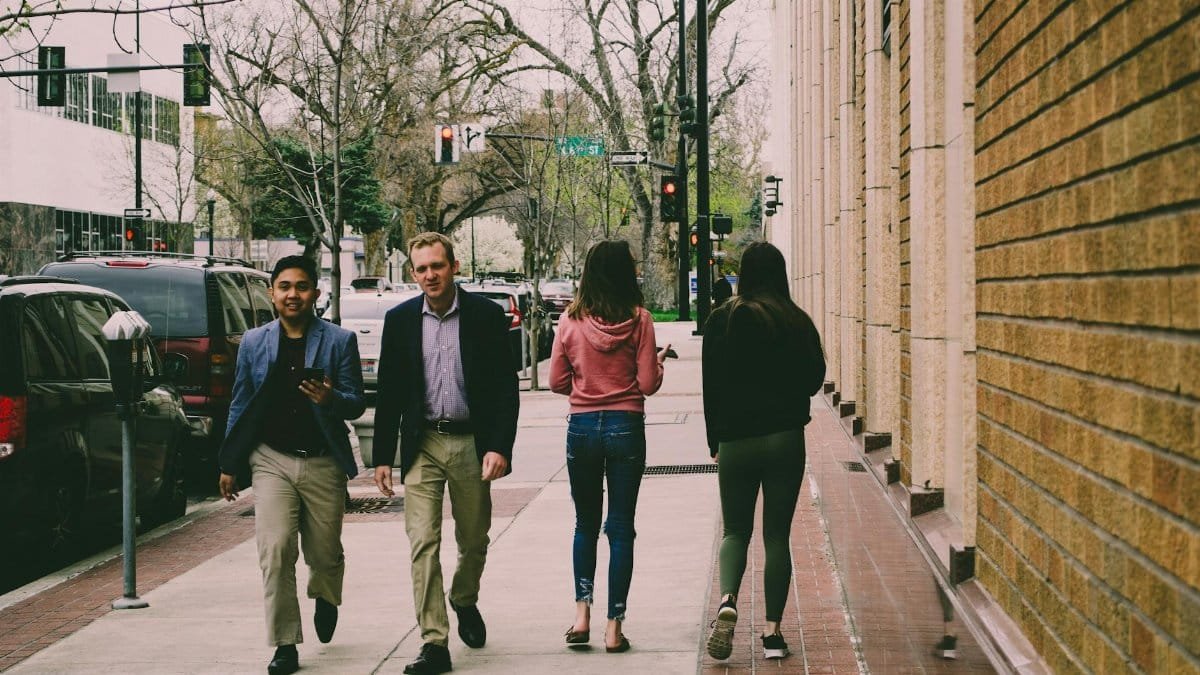 Four adults walking on a city sidewalk during the day, with vibrant urban scenery.