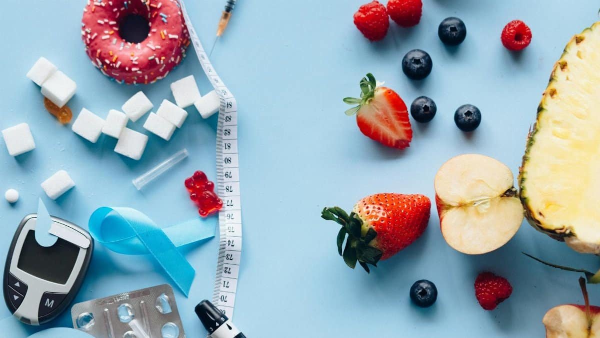 Flatlay of fruits, sugary treats, and diabetes tools on a blue background, symbolizing health choices.