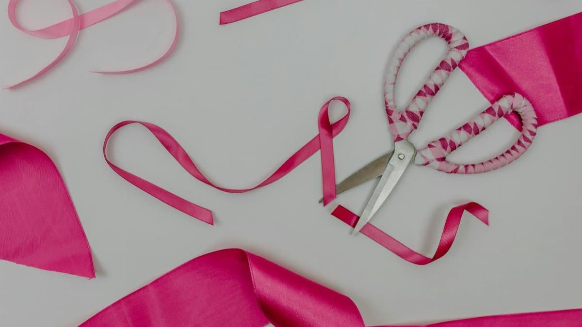 Pink ribbon and scissors on white surface symbolizing breast cancer awareness and support.