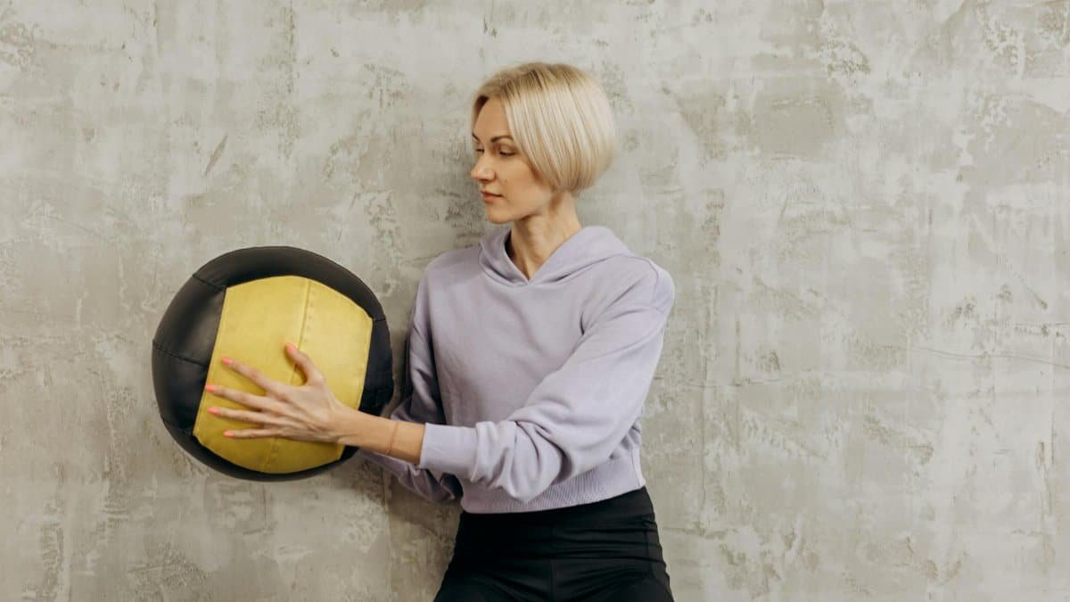 Woman in athletic wear practicing with a medicine ball indoors, showcasing strength and concentration.