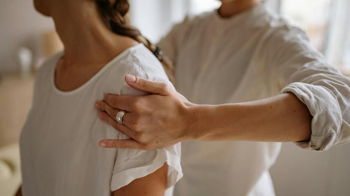 A detailed view of a physiotherapy session with hand placement on shoulder indoors.