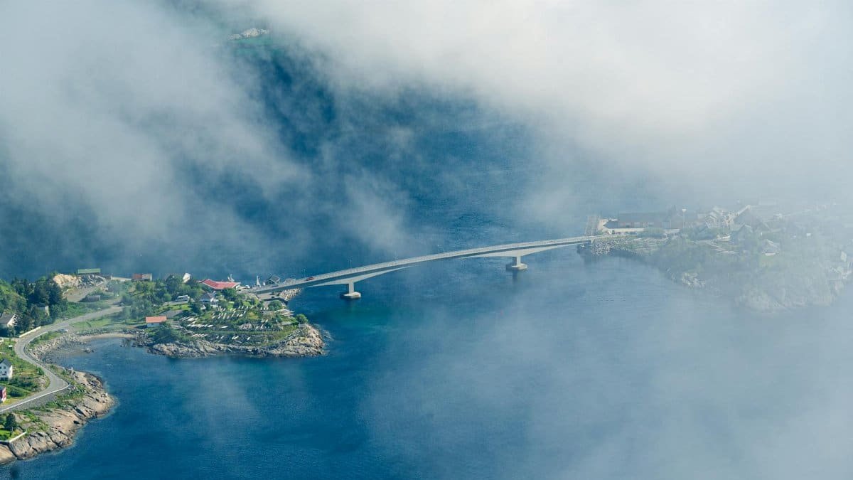 Aerial shot of Reine, Norway with a bridge amidst clouds, showcasing a coastal landscape.