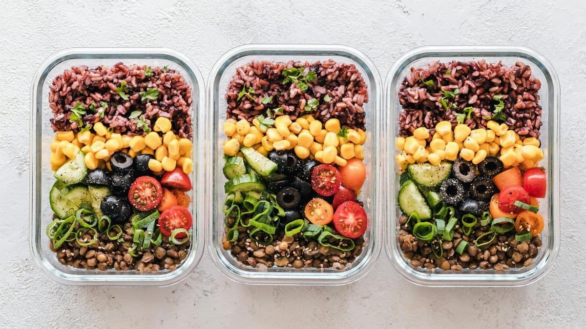 Colorful healthy meal prep with corn, olives, tomatoes, and lentils in glass containers. Perfect for mindful eating.