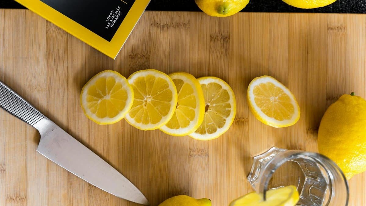 Overhead view of sliced lemons and knife on a wooden board, perfect for refreshing lemonade or culinary use.