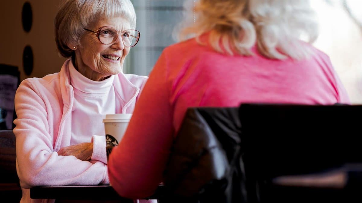 Senior women sharing a joyful conversation over coffee in a cozy indoor setting.