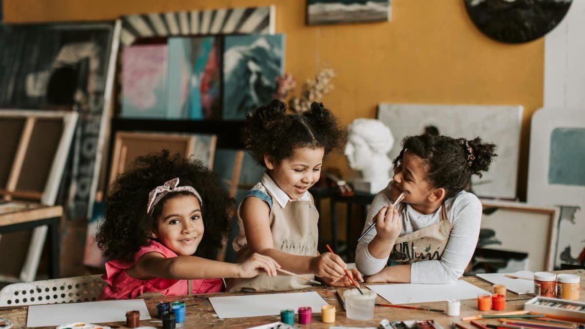 Three children enjoying a creative painting session in an art workshop, surrounded by colorful paints and brushes.