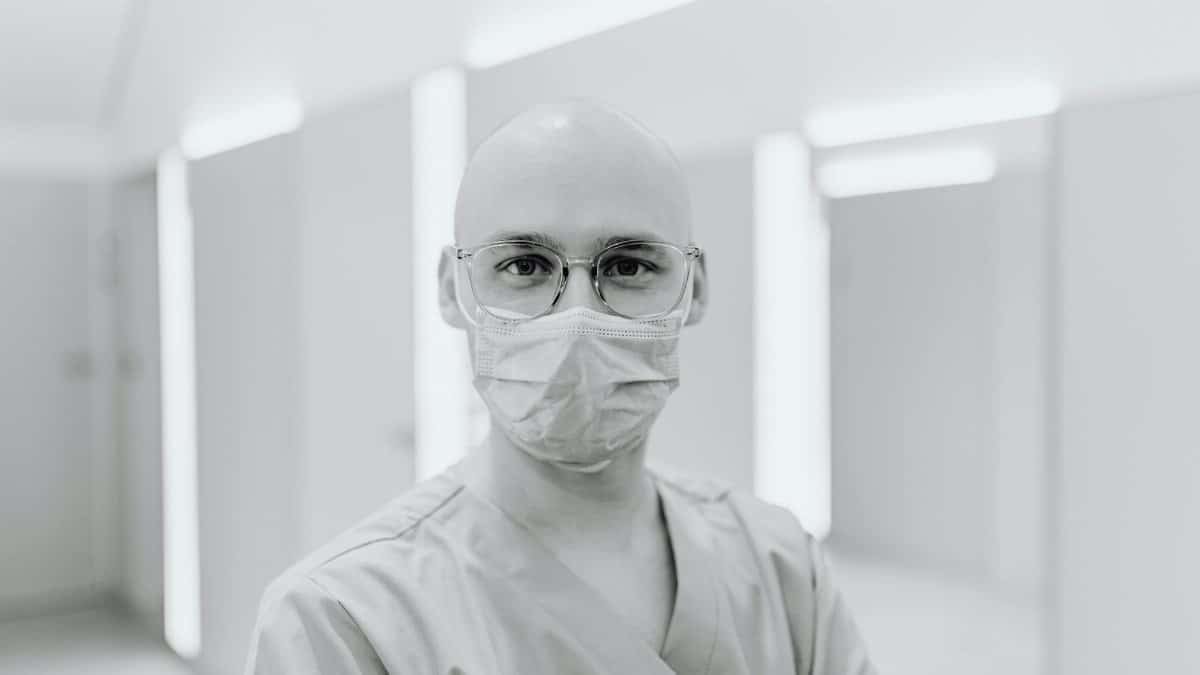 Bald healthcare worker wearing glasses and mask inside a modern facility.